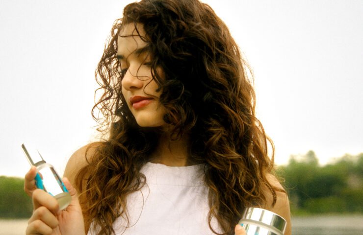 Woman with wavy curls holding Müllwood Hydrating Hair Mist and Lasting Curl Gel by a lake at sunset